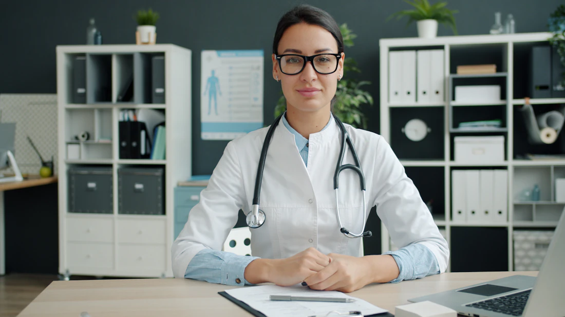 A friendly GP seated at her desk in a bright consulting room
