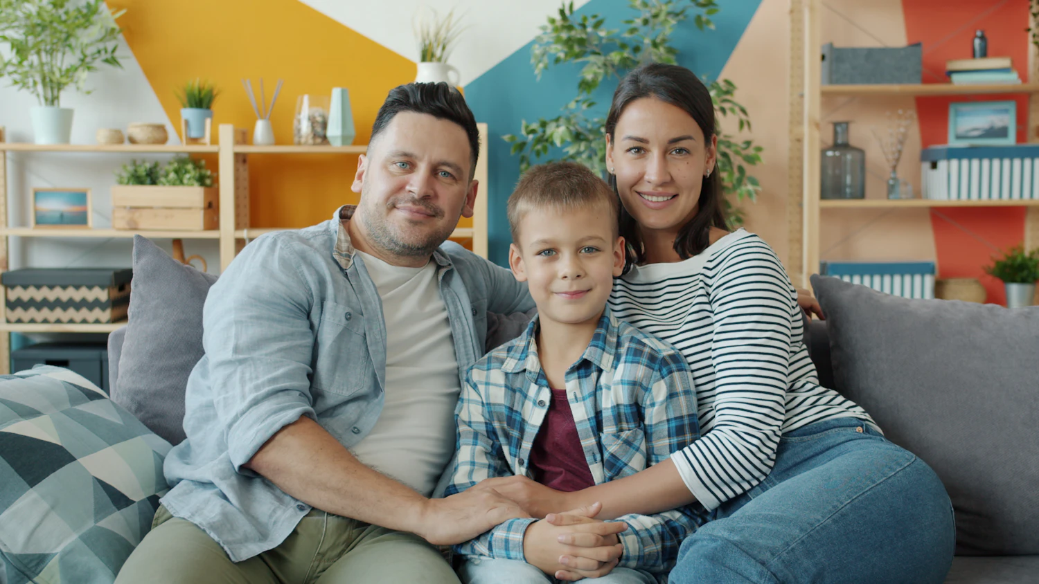 A smiling family of three sitting together on a sofa